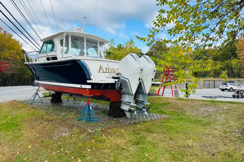 Amanda Yacht Photos Pics 2024 Back Cove 34O boat on stands, dual outboard engines, parked near trees and road.