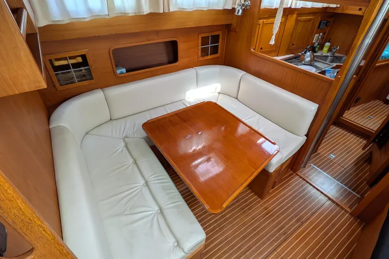 Firefly Yacht Photos Pics Cozy dining area in 1985 Siltala Nauticat 44 yacht with wooden table and white seating.