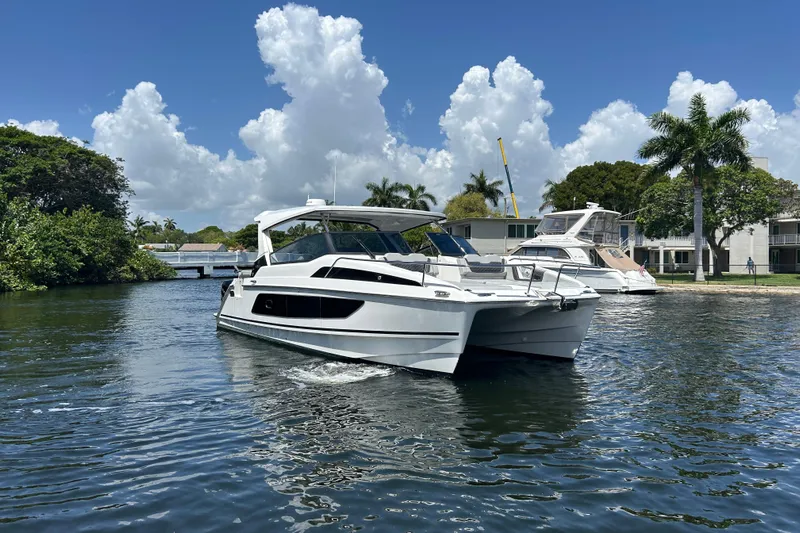  Yacht Photos Pics 2020 Aquila 36 Sport catamaran cruising on a sunny day with palm trees in the background.