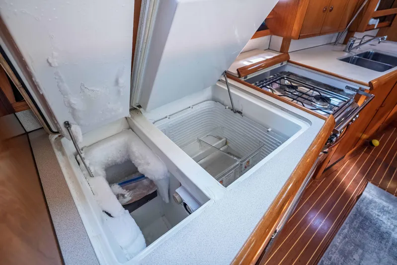 "champagne" Yacht Photos Pics Jeanneau Sun Odyssey 45.2 yacht kitchen with open freezer, stove, and wooden cabinetry.