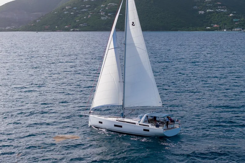 Heartbeat Yacht Photos Pics 2024 Beneteau Oceanis Yacht 54 sailing on open water with lush green hills in background.
