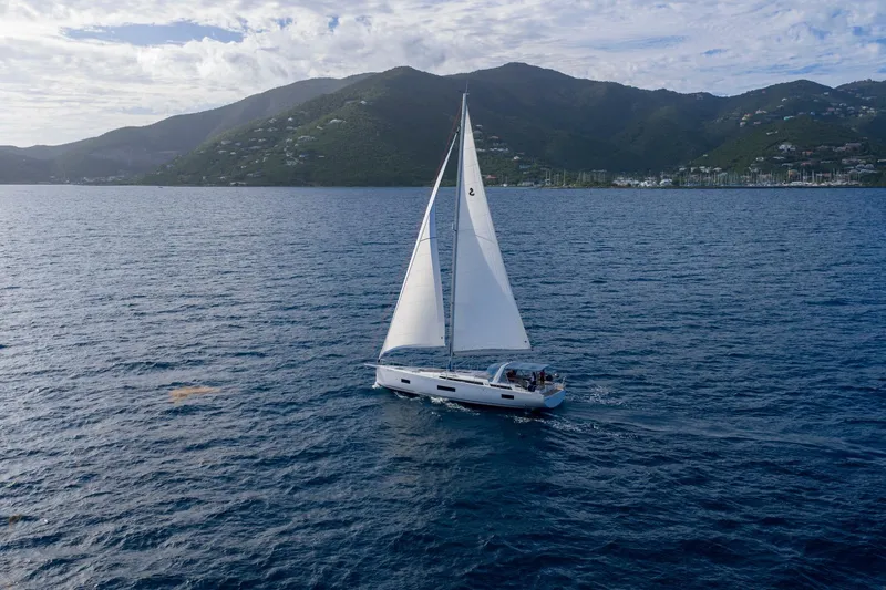 Heartbeat Yacht Photos Pics 2024 Beneteau Oceanis Yacht 54 sailing near mountainous coastline under cloudy sky.