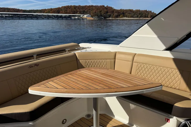  Yacht Photos Pics 2026 Sea Ray SLX 310 boat interior with tan seating and wooden table on a calm lake.