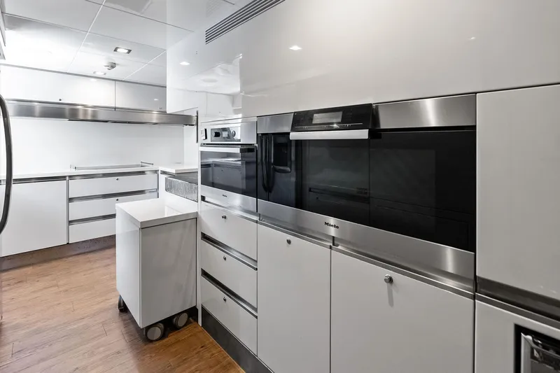Sha Sha Sha IV Yacht Photos Pics Modern yacht kitchen with sleek white cabinetry, stainless steel appliances, and wood flooring, Custom Line 100.