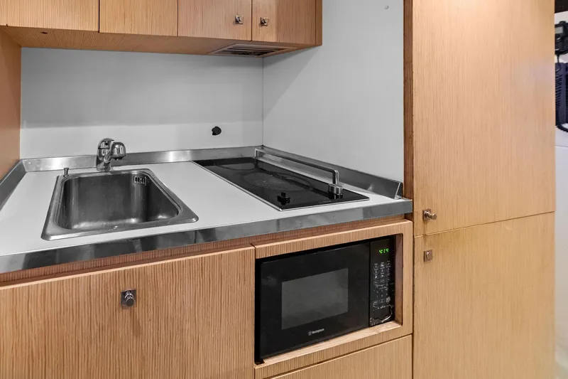 Sha Sha Sha IV Yacht Photos Pics Compact kitchen area with sink, stove, and microwave in a 2014 Custom Line 100 model.