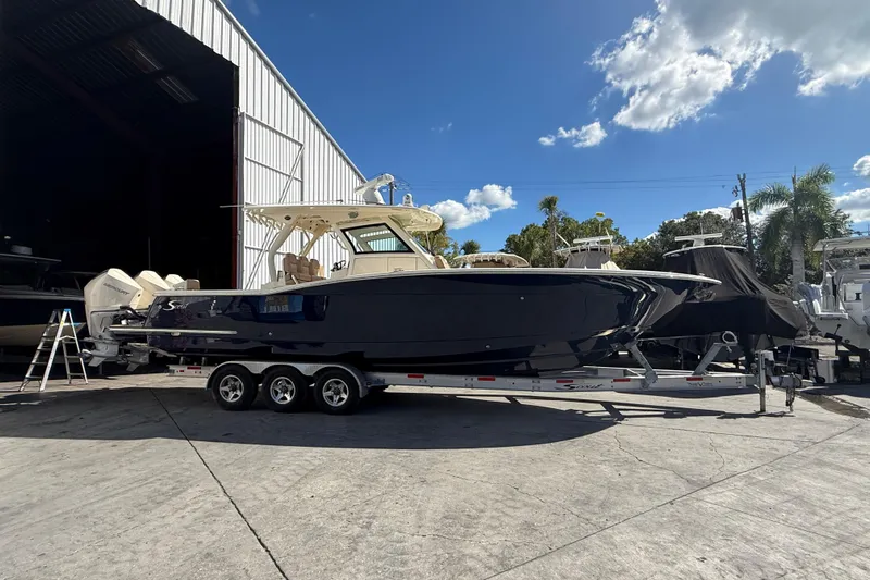  Yacht Photos Pics 2022 Scout 355 LXF boat on trailer outside a storage facility under a clear blue sky.