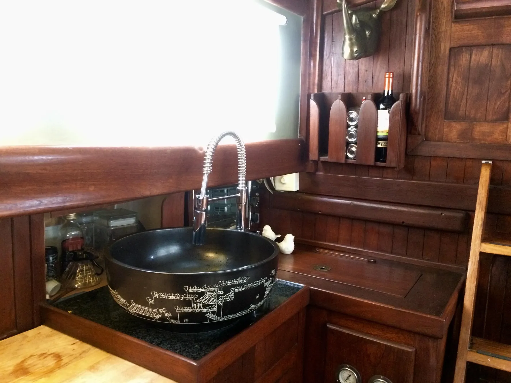 Vintage 1971 Formosa 41 yacht kitchen with wooden cabinetry and decorative black sink.