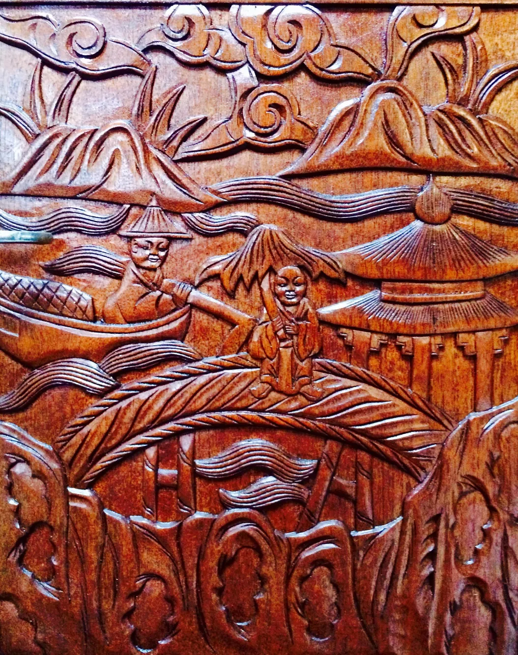 Intricately carved wooden panel depicting traditional Asian scenery, featuring mountains and figures in a boat.