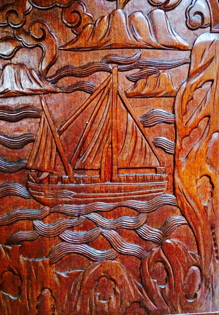 Intricate wooden carving of a sailboat, Formosa 41, 1971, with waves and mountains.