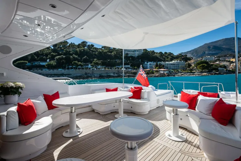 Yacht Photos Pics Luxurious 2004 Mangusta 108 yacht deck with white seating, red cushions, and scenic coastal view.