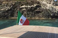 Maxi Custom Tender 1996 boat with flag, near rocky shoreline and clear water.