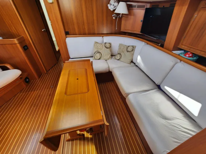 Just Do It Yacht Photos Pics Interior of 2006 Hallberg-Rassy 53 yacht with wooden table and white cushioned seating.