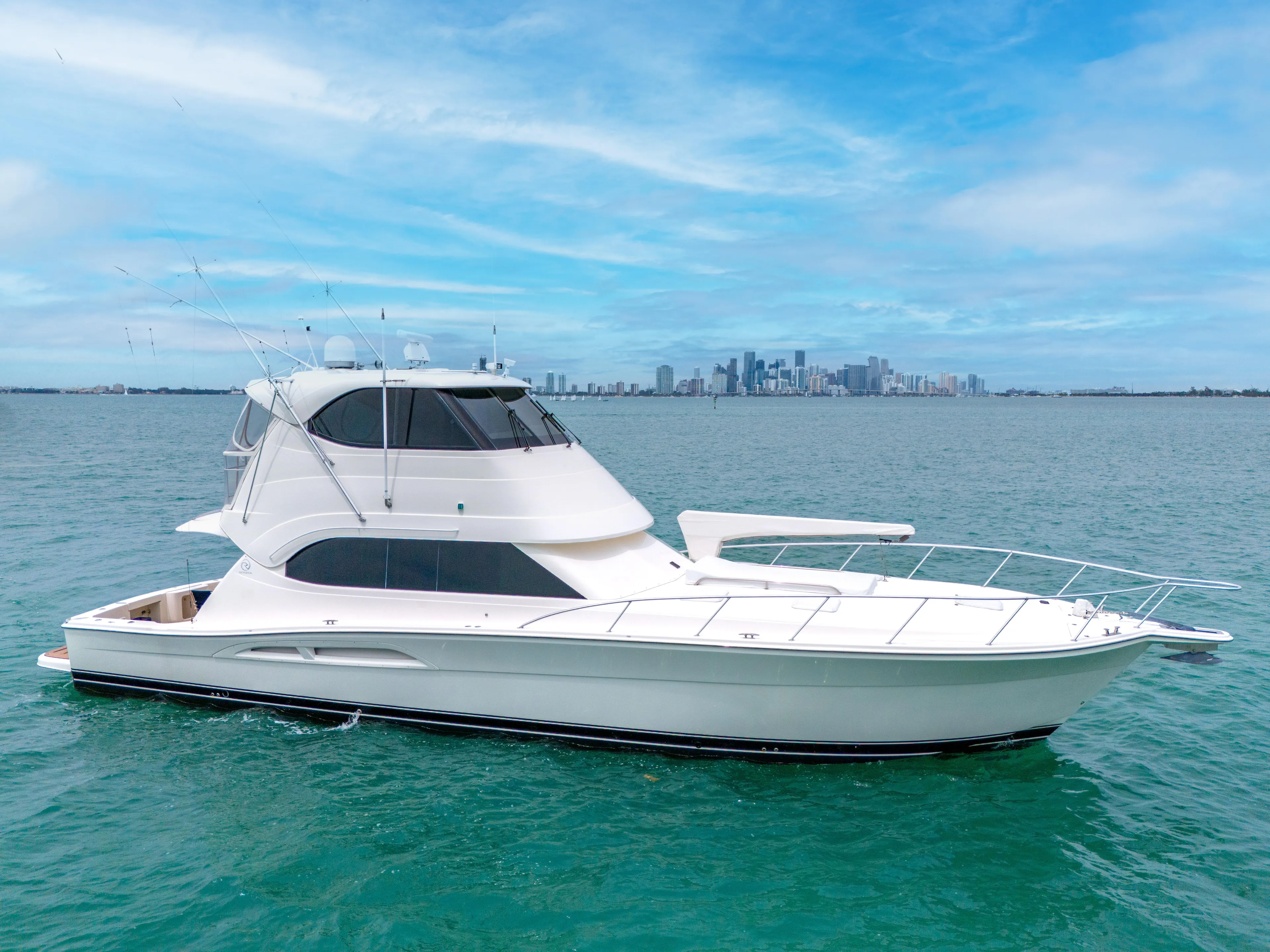  Yacht Photos Pics 2008 Riviera 51 Enclosed Bridge yacht on blue water with city skyline background.