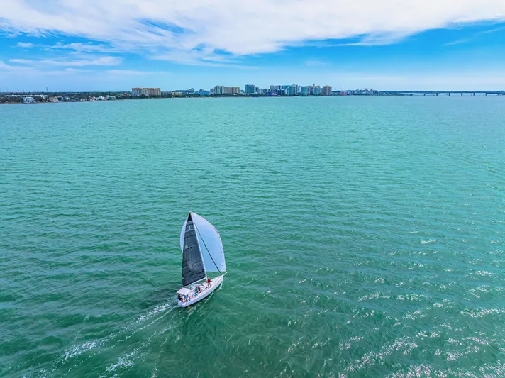 Encore Yacht Photos Pics Sailboat J/95 cruising on turquoise waters, cityscape in background, under a partly cloudy sky.