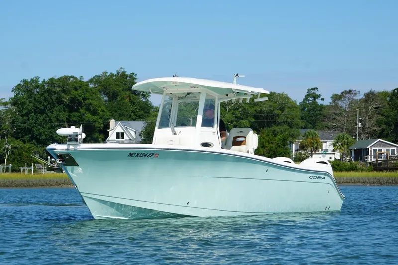  Yacht Photos Pics 2020 Cobia 280 Center Console boat on calm water, surrounded by lush greenery.