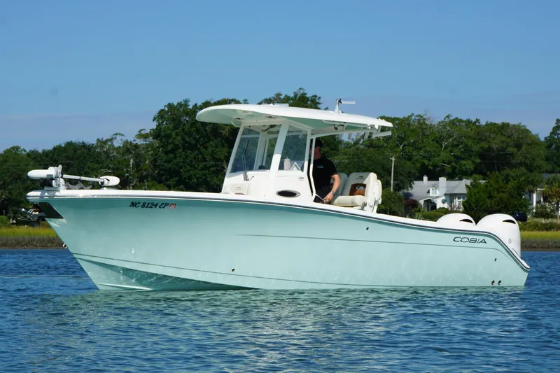  Yacht Photos Pics 2020 Cobia 280 Center Console boat on calm water, with trees in the background.