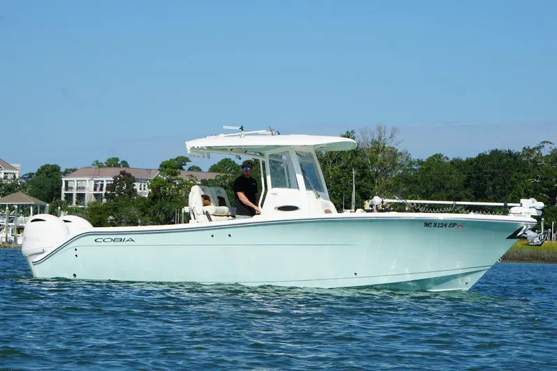  Yacht Photos Pics 2020 Cobia 280 Center Console boat on water, with trees and buildings in the background.