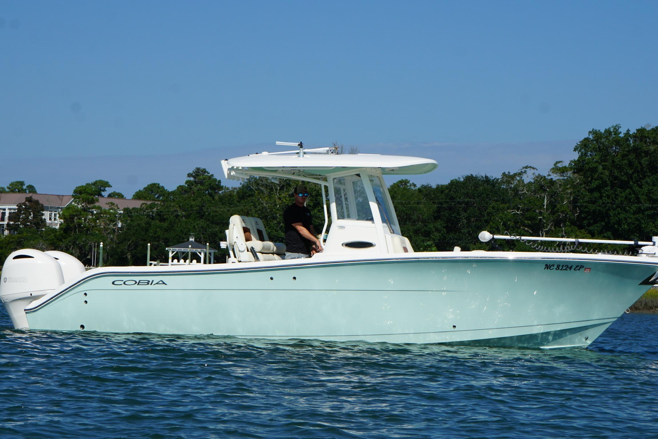 2020 Cobia 280 Center Console boat on water, clear sky, lush greenery background.
