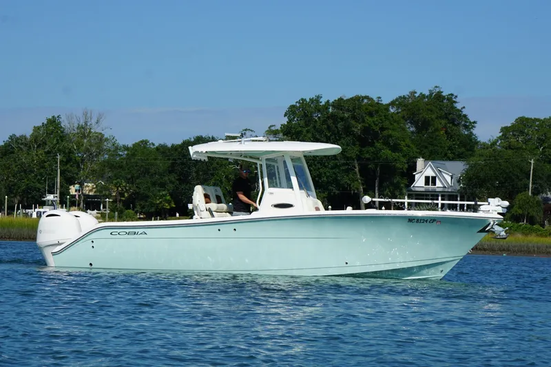  Yacht Photos Pics 2020 Cobia 280 Center Console boat cruising on a calm lake with trees in the background.