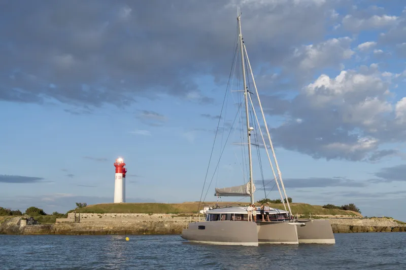 Dauntless Yacht Photos Pics Sailing catamaran NEEL 51 near a lighthouse under a partly cloudy sky.