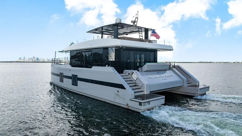 Island Majesty Yacht Photos Pics Luxurious 2018 Sunreef 70 yacht cruising on open water with city skyline in background.