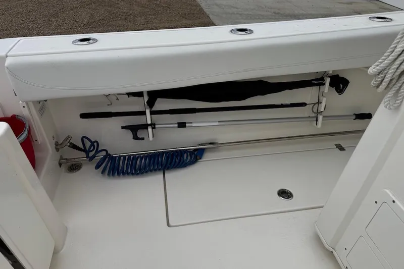  Yacht Photos Pics 2023 Cobia 301 Center Console boat storage compartment with fishing gear and coiled hose.