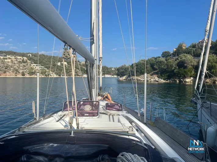  Yacht Photos Pics Beneteau Oceanis 46 sailboat on calm waters, surrounded by lush greenery, under a clear blue sky.
