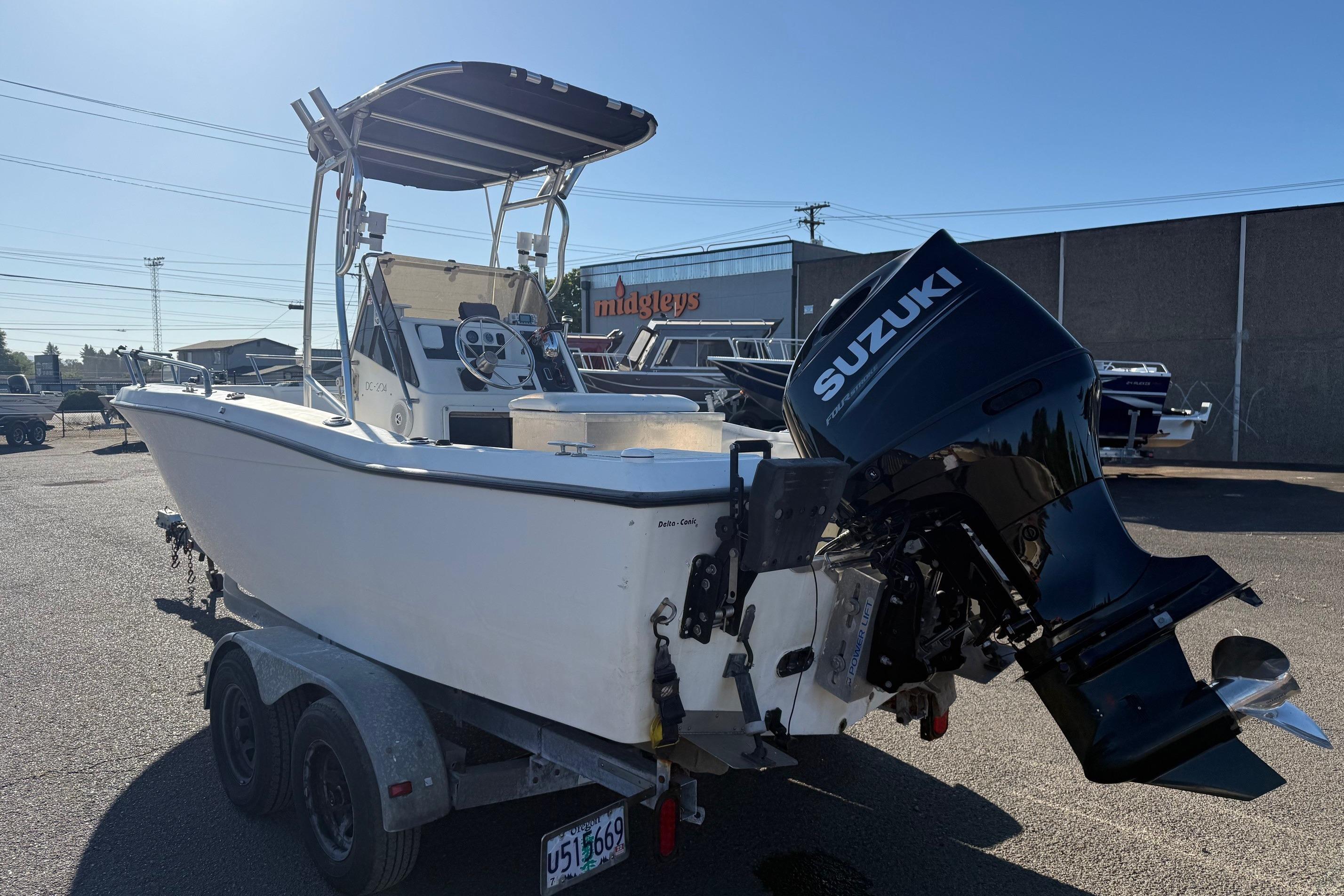 1990 Larson DC-204 boat on trailer with Suzuki outboard motor in parking lot.
