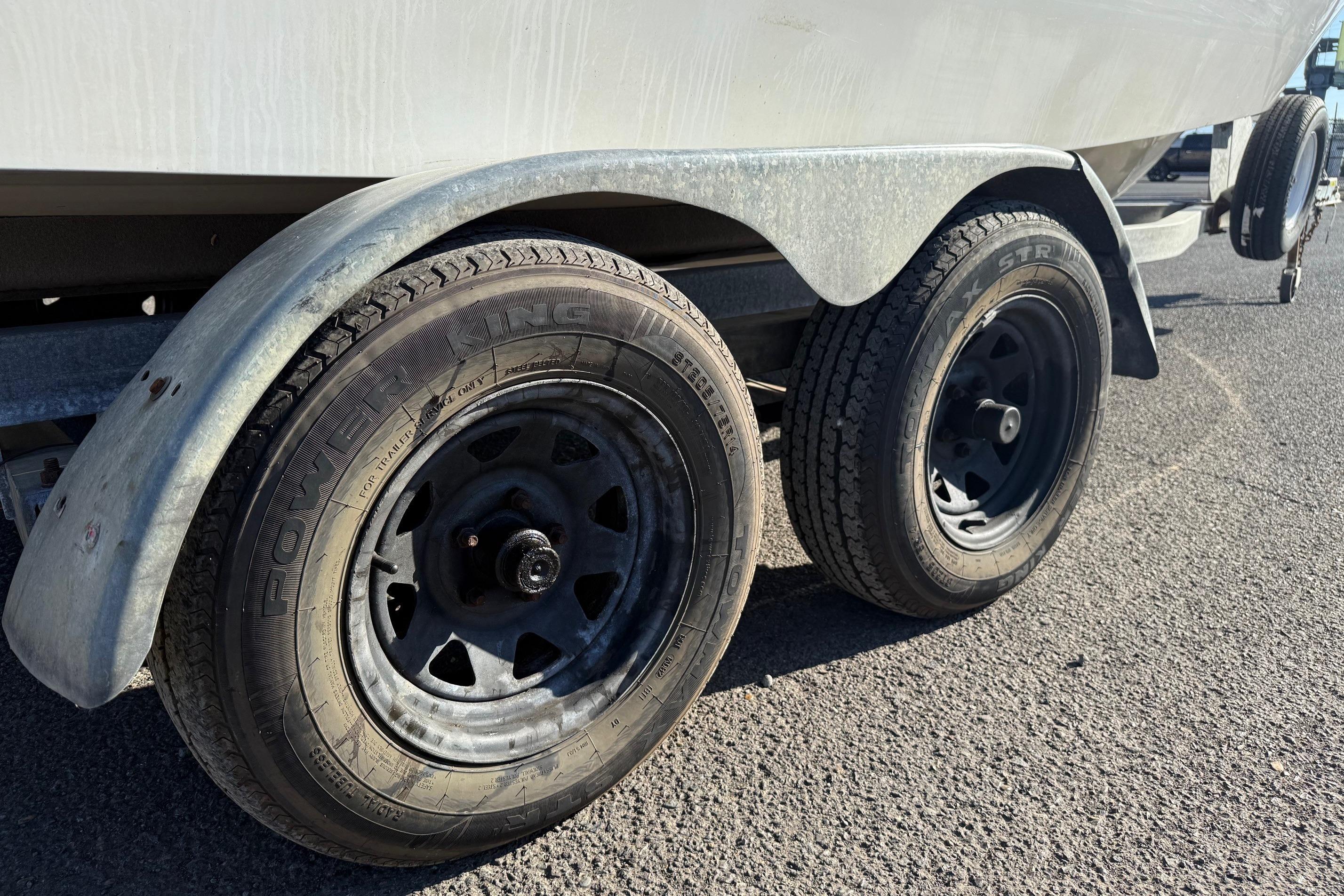 Trailer wheels of a 1990 Larson DC-204 boat on asphalt surface.