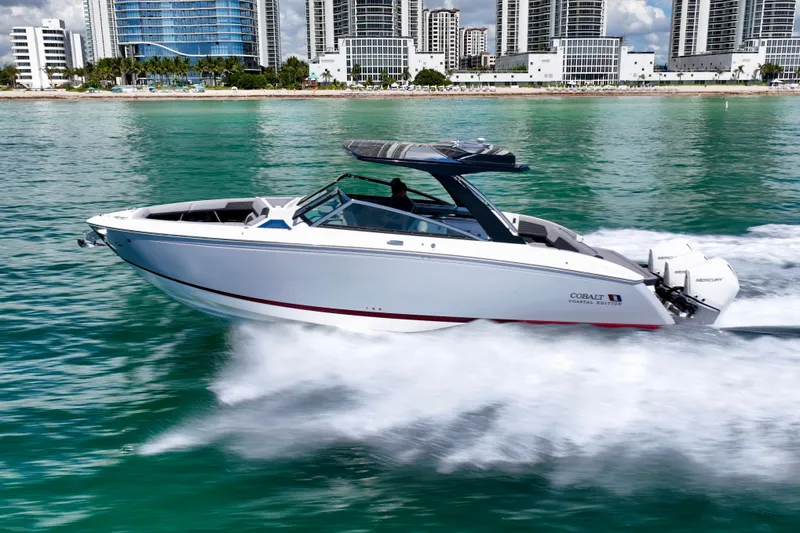  Yacht Photos Pics 2025 Cobalt R33 Outboard boat cruising on turquoise water near modern cityscape.
