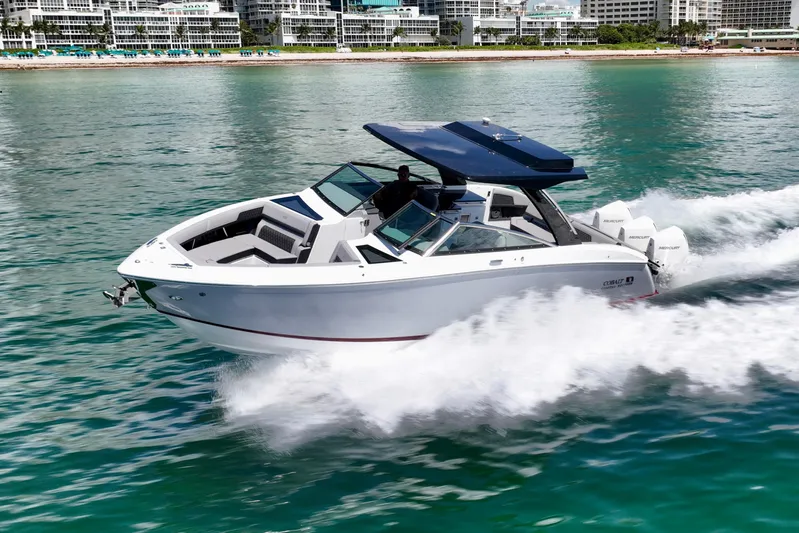  Yacht Photos Pics 2025 Cobalt R33 Outboard boat cruising on clear blue water near a city shoreline.
