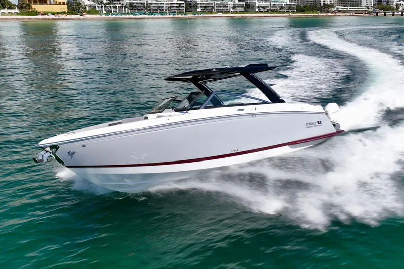  Yacht Photos Pics 2025 Cobalt R33 Outboard boat cruising on clear blue water near a city shoreline.