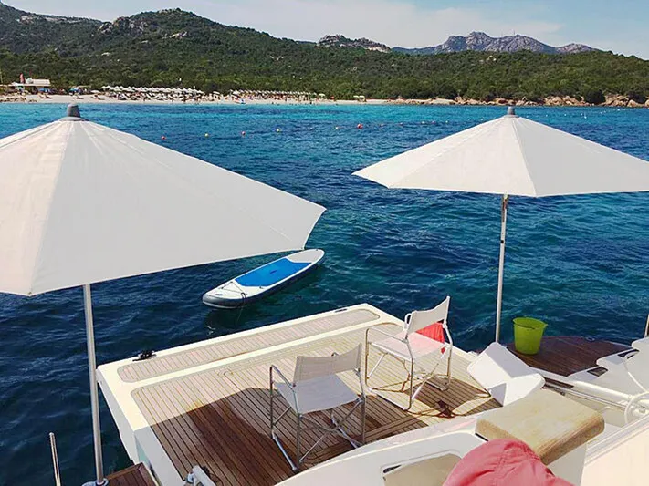  Yacht Photos Pics Luxurious 2017 Custom Line Navetta 28 yacht deck with umbrellas, chairs, and paddleboard on serene water.