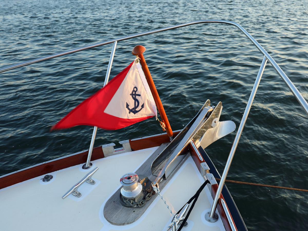 Bow of 1995 Able 44 boat with anchor flag on calm water.
