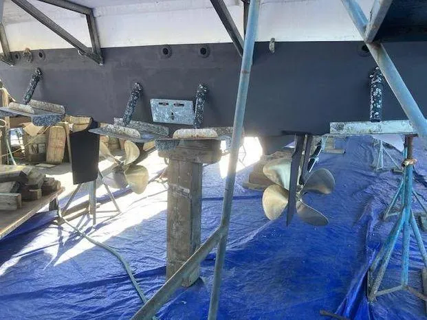 Magna Veritas Yacht Photos Pics 1996 Bayliner 4788 yacht under maintenance, showing propellers and hull on a blue tarp.