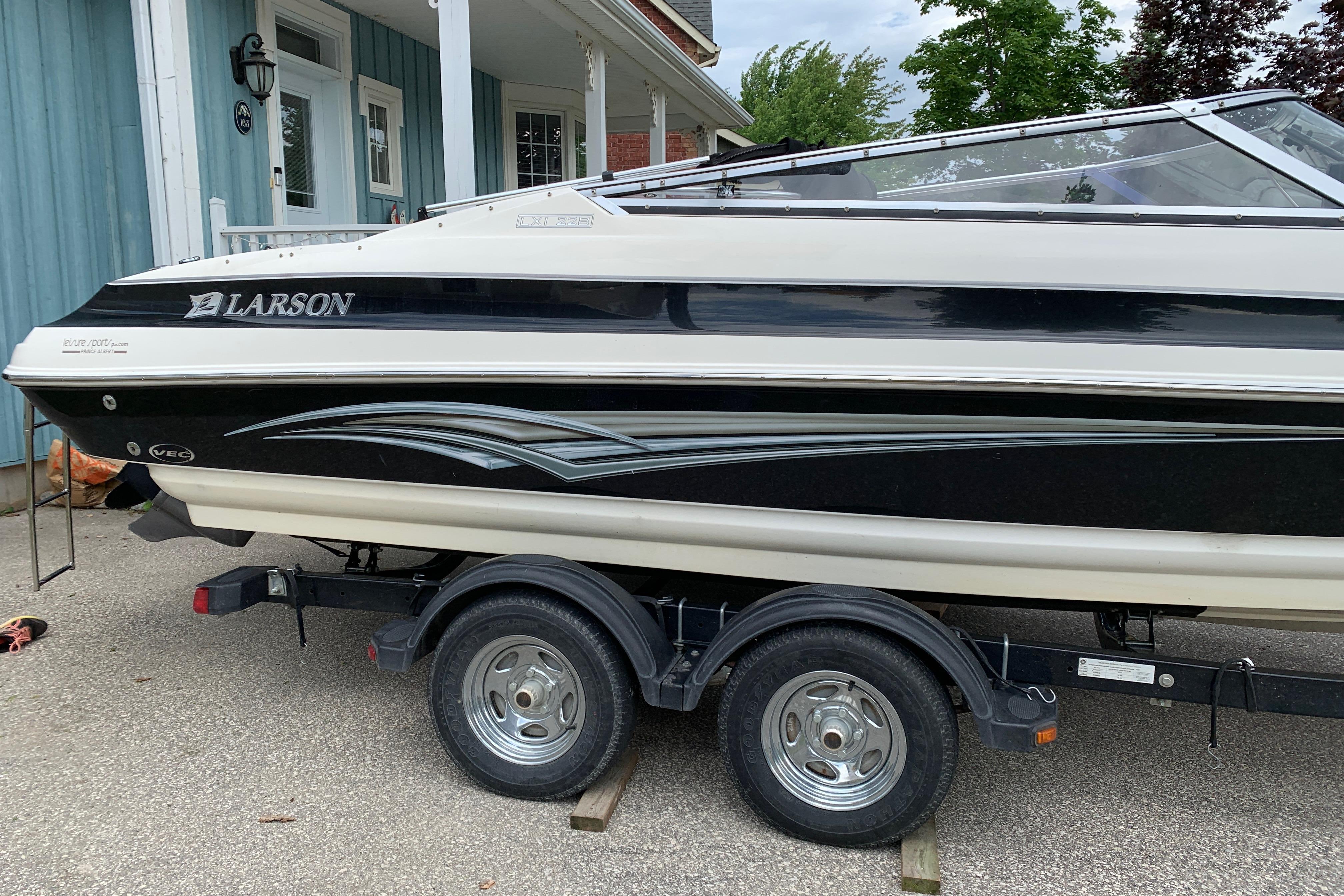 2006 Larson LXi 228 boat on trailer, parked near a house.
