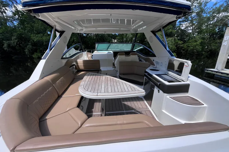Blu Yacht Photos Pics 2020 Sea Ray Sundancer 320 Outboard interior with seating and kitchenette, docked by lush greenery.