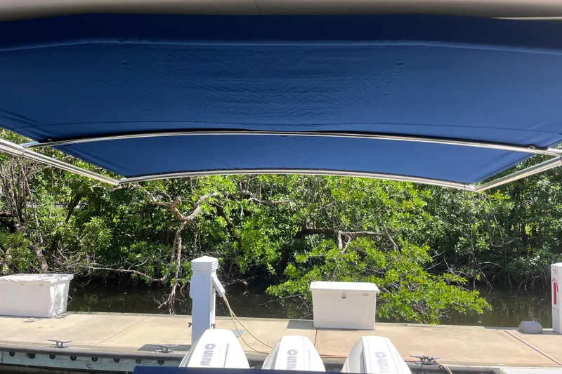 Blu Yacht Photos Pics 2020 Sea Ray Sundancer 320 Outboard with blue canopy docked near lush greenery.