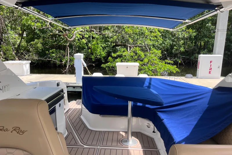 Blu Yacht Photos Pics 2020 Sea Ray Sundancer 320 Outboard interior with blue canopy and seating, docked near lush greenery.