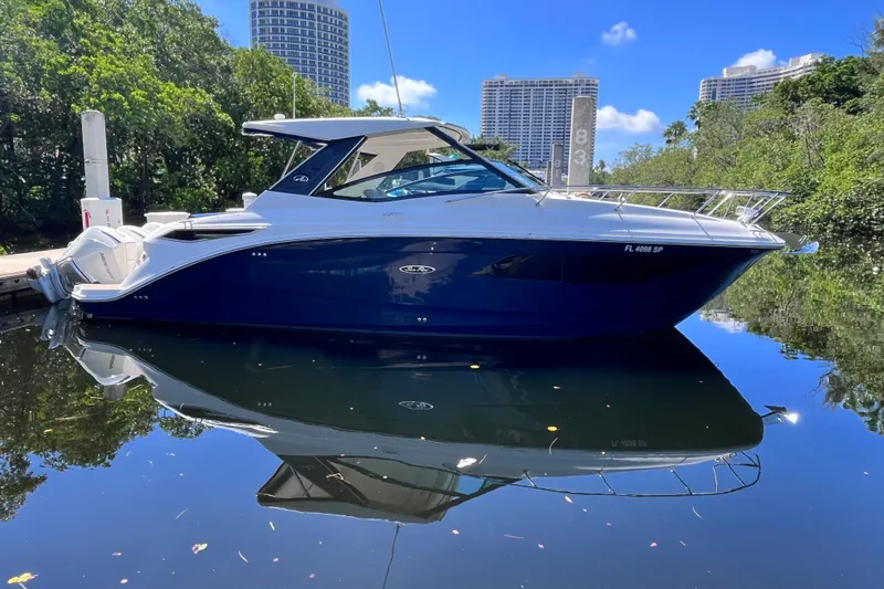 Blu Yacht Photos Pics 2020 Sea Ray Sundancer 320 Outboard yacht docked on calm water, surrounded by greenery.