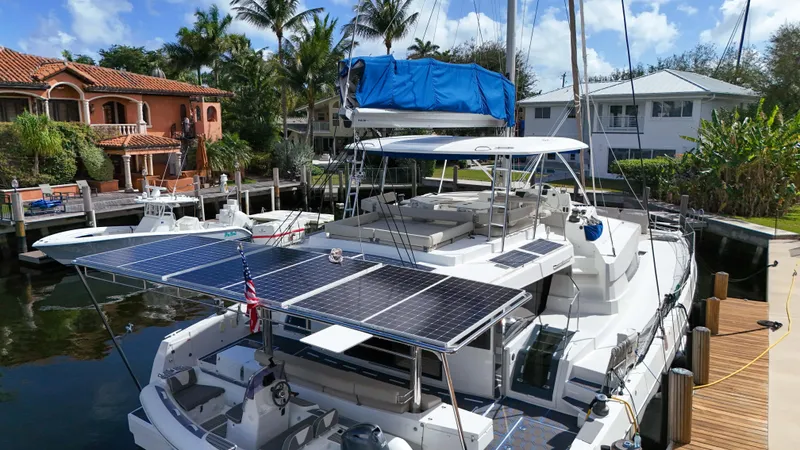 Joy Yacht Photos Pics Bali 5.4 catamaran docked, featuring solar panels, surrounded by tropical homes and palm trees.