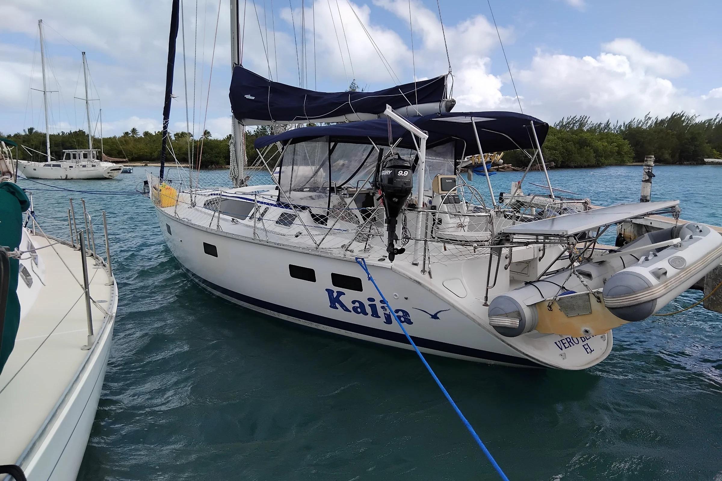 Sailboat "Kaija" docked, 1994 Hunter Legend 40.5, calm waters, clear sky, lush background.
