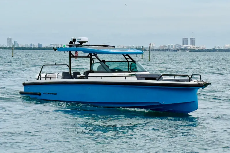 Out Of The Blue Yacht Photos Pics 2021 Axopar 37 Sun Top boat cruising on open water with city skyline backdrop.