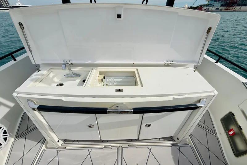 Out Of The Blue Yacht Photos Pics 2021 Axopar 37 Sun Top boat kitchenette with sink and storage, docked by the water.