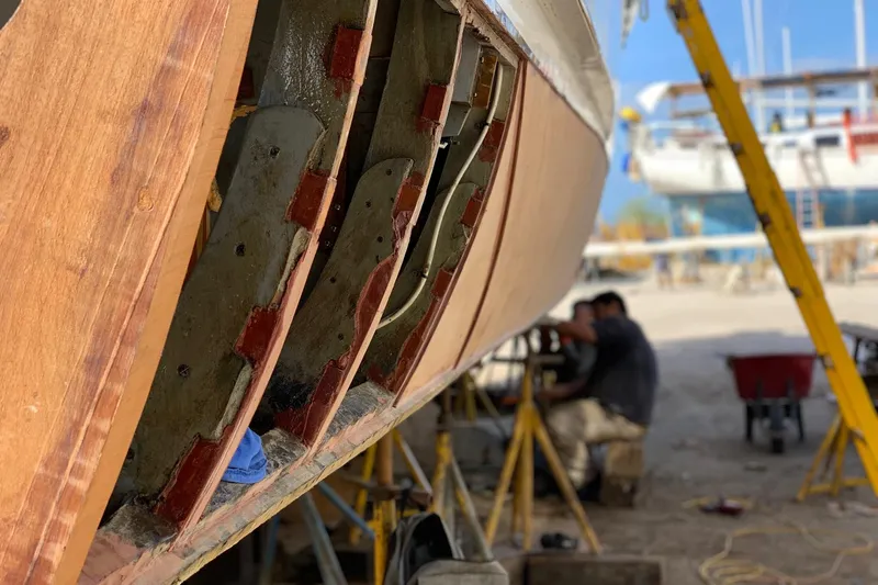 New School Yacht Photos Pics 1966 Chris-Craft Constellation undergoing restoration, with visible hull repairs and worker in background.