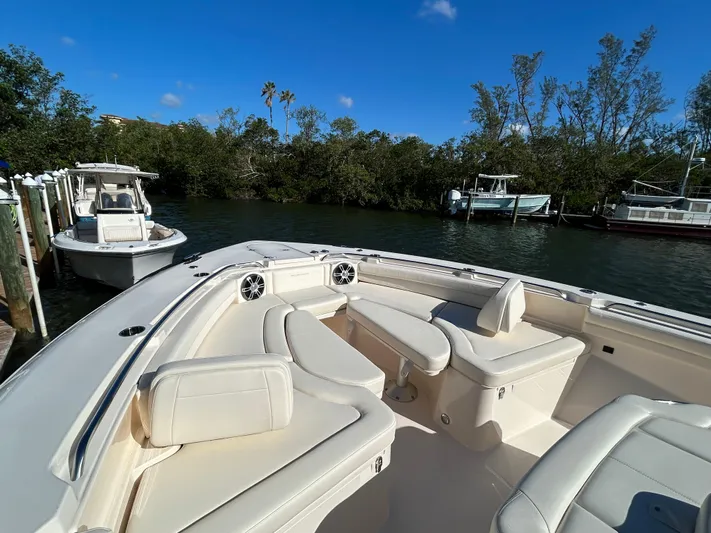  Yacht Photos Pics 2024 Grady-White Canyon 456 boat with luxurious seating, docked near lush greenery.