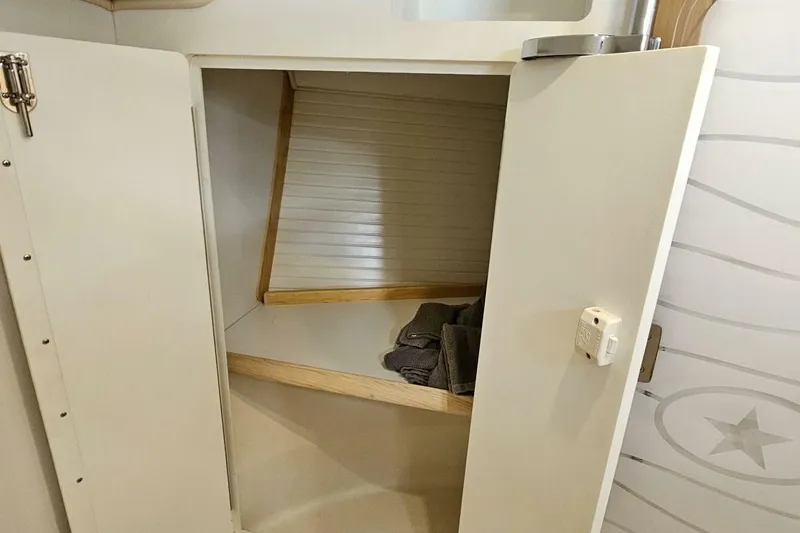  Yacht Photos Pics Open storage cabinet inside 2023 Island Packet 439 sailboat, featuring wooden shelves and folded towels.