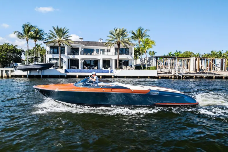 Isola Yacht Photos Pics 2013 Riva 33 Aquariva cruising on water near luxury waterfront home with palm trees.