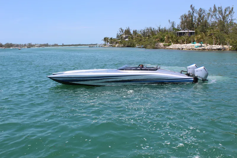  Yacht Photos Pics 2025 Fountain 34 Thundercat speedboat on clear blue water, near a lush shoreline.