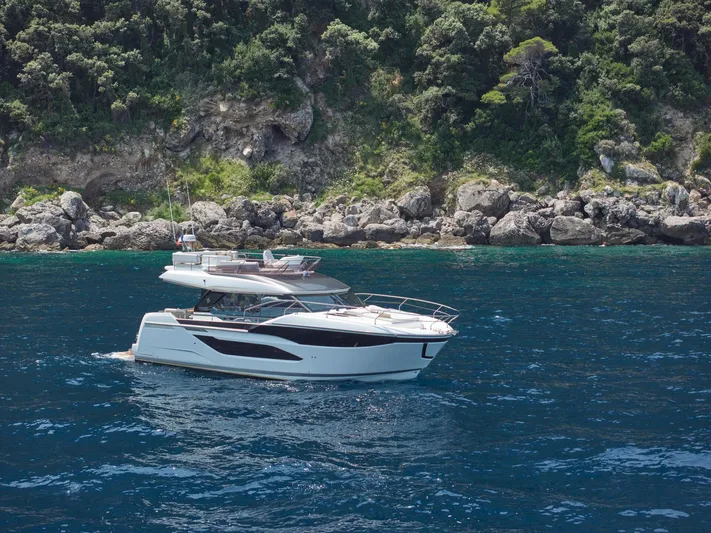  Yacht Photos Pics 2025 Prestige F 4.9 yacht cruising near rocky coastline with lush greenery.